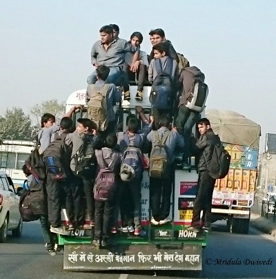 People hanging from a bus in a city in India
